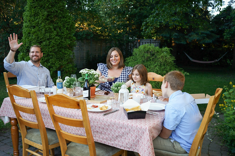 Family of four sitting at dinner table in backyard